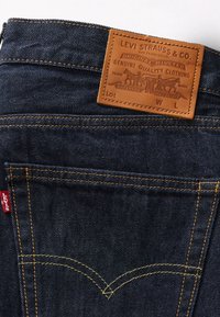 Poche arrière de jean en denim bleu foncé avec surpiqûres jaunes et un patch en cuir marron Levi Strauss & Co. au-dessus.