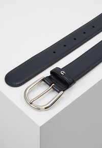 Cinturón de cuero azul marino con hebilla rectangular plateada, que presenta múltiples agujeros para ajustes, colocado sobre un fondo neutro.