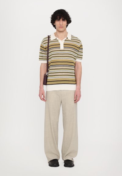 Polo a righe in verde, marrone e crema, con colletto e maniche corte. Abbinato a pantaloni beige chiaro a gamba larga e scarpe nere.