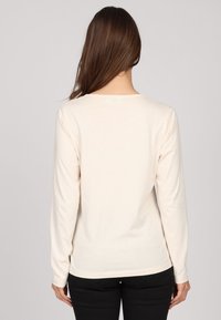 Haut à manches longues de couleur crème en coton doux. Il présente un col rond et un ourlet légèrement incurvé. Aucun motif ni accent visible.