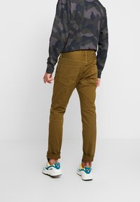 Brązowe bawełniane chinosy o slim fit, z podwiniętymi mankietami, dwiema tylnymi kieszeniami i gładką teksturą, połączone z kolorowymi trampkami.