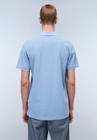 Lyseblå kortermet polo-skjorte med ribbet krage, subtil tekstur og en liten logo-akcent i rødt og blått på baksiden.
