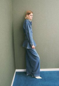 Giacca in denim con design peplum, abbinata a pantaloni in denim a gamba larga. Colore azzurro chiaro, con tasche e dettagli hardware minimi.