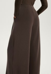 Bruine wijde broek met verticale witte streepjes, voorzien van zijzakken en een gladde, gestructureerde stof voor flexibiliteit.