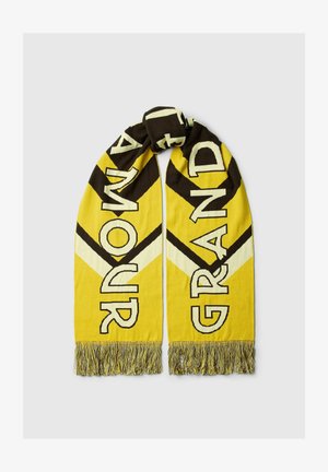 Sárga és fekete kötött sál széles átlós csíkokkal és rojtos végekkel, mindkét oldalán vastag betűkkel "RUNOMA" és "GRAND" felirattal.