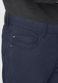 Navy blue denim jeans with a textured finish, featuring a front pocket, stitched accents, and a small logo on the front pocket.