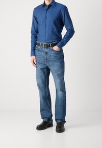 Niebieska koszula z długim rękawem z guzikami w połączeniu z jasnoniebieskimi dżinsami i czarnym paskiem. Czarny obuwie dopełnia strój, prezentując swobodny, dopasowany wygląd.