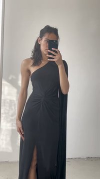Rochie neagră cu un umăr, cu un detaliu de nod răsucit la talie, fante pe laterale, textură netedă și o extensie fluidă asemănătoare unei capele.