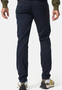 Pantalon bleu marine à coupe slim, fabriqué en tissu coton lisse. Présente des poches avant et arrière, et un design uni. Porté avec des chaussures de sport.