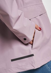 Heled hallikas vihmakaitsevari, millel on must nupp ja küljetasku, mille alläärel on must aktsenttriip. Sile tekstuur.