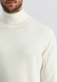 Cremefarbener Rollkragenpullover aus feinem Strickstoff, mit hohem Kragen, gerippter Textur und einem glatten, minimalistischen Design.
