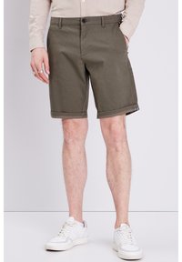 Olivgröna shorts i en texturerad tyg, med knappstängning och rullad nederkant. Bärs med vita sneakers.
