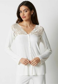 Hvid langærmet bluse med blonde yoke, v-halsudskæring, knaplukning foran og en blød tekstur. Simple design med en flatterende pasform.