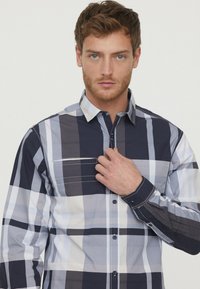 Langermige geruite shirt in marineblauw, grijs en wit. Zachte stof, knoopsluiting bij de kraag, één borstzak en contrasterende stiksels.