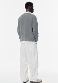 Maglione grigio a coste con colletto bianco, abbinato a pantaloni bianchi larghi. L'outfit presenta una vestibilità rilassata e tasche posteriori visibili.