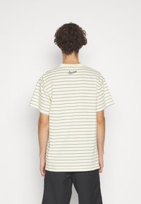 Randig t-shirt med kort ärm i ljusgul med marinblå horisontella linjer, med en liten svart logotyp vid nackområdet.