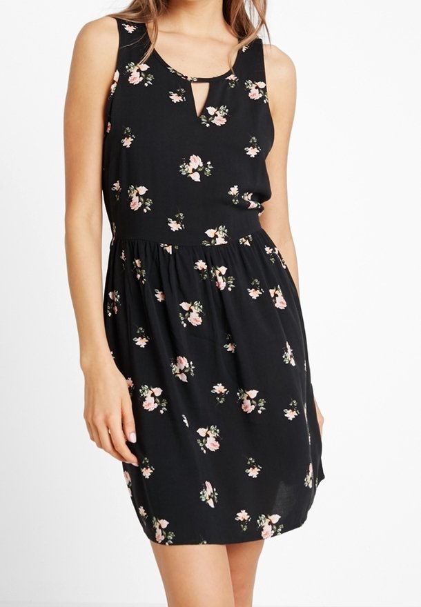 Ärm Lös svart klänning med samlad midja och små rosa blommor, bärs av en stående person från halsen till mitten av låret.