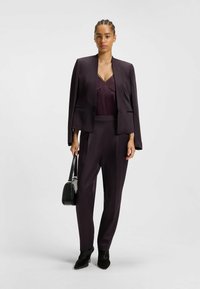 Donkerpaarse blazer met vloeiende mouwen, bijpassende hooggesneden broek en een donker bordeaux satijnen top met kantaccenten. Zwarte handtas en enkellaarsjes.