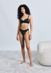 Black lace lingerie set featuring a bralette with scalloped edges and matching thong. Smooth texture with delicate floral patterns.