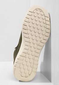 Zapatillas de deporte verde olivo con un upper de tejido texturizado, que cuentan con una suela de goma con un patrón de tracción hexagonal.