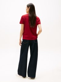 Camiseta roja de manga corta combinada con jeans de mezclilla oscura de pierna ancha. El conjunto presenta un diseño minimalista y una textura suave.