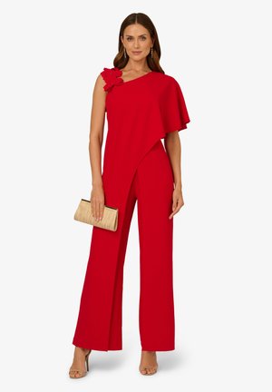 Roter Jumpsuit mit asymmetrischem Ein-Schulter-Design, floraler Akzent an der Schulter, weitem Bein und glattem Stoff; kombiniert mit einer goldenen Clutch.