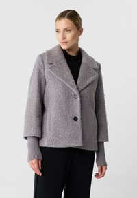 Giacca in misto lana grigio chiaro, con texture, ampi rever, due bottoni neri e polsini a costine; taglio oversize, adatta per essere indossata a strati.