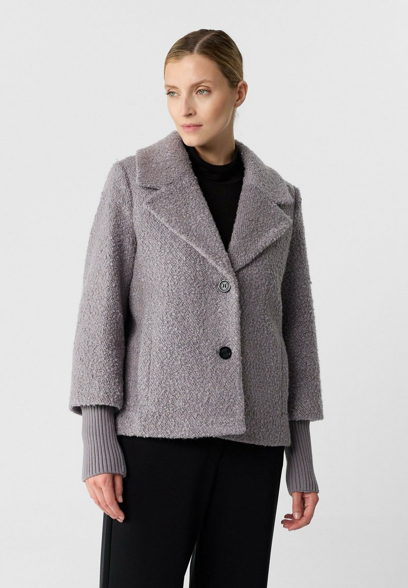 Giacca in misto lana grigio chiaro, con texture, ampi rever, due bottoni neri e polsini a costine; taglio oversize, adatta per essere indossata a strati.