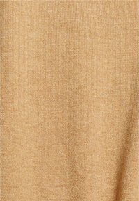 Gros plan sur un tissu tricoté doux de couleur fauve avec une texture fine, uniforme et un motif chiné subtil.