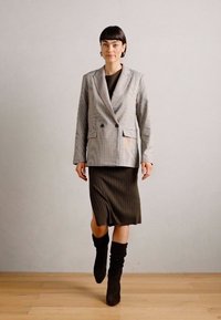 Šedý kostkovaný blazer s dvouřadým zapínáním, doplněný o proužkované midi šaty olivové barvy a hnědé nubukové boty nad kolena.