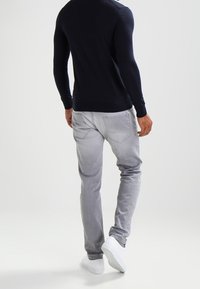 Marinblå tröja och ljusgrå byxor. Tröjan är figurnära med rund hals. Byxorna är avsmalnande med bakfickor. Vita sneakers fulländar looken.