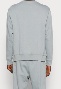 Ljusgrå sweatshirt i mjukt tyg; har ett ribbat krage och muddar, och en något lös passform med en ren design.