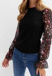 Zwarte top met doorzichtige, bloemenbedrukte mouwen en een gerimpelde zoom. Klassieke pasvorm in combinatie met een spijkerbroek, wat een casual stijl uitstraalt.