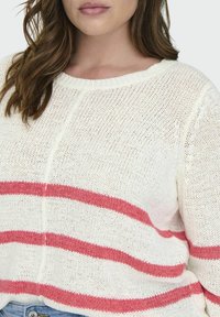 Maglione bianco lavorato a maglia con ampie strisce rosa sulla parte anteriore e scollatura rotonda a costine. La texture sembra morbida e leggera.