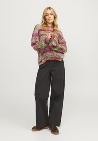 Maglione lavorato a maglia con un motivo multicolore in rosa, verde e viola, abbinato a pantaloni neri larghi a vita alta e scarpe stringate marroni.