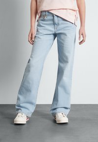 Světle modré široké džíny z denimu s vintage efektem praní a standardním designem s pěti kapsami, doplněné bílými teniskami.