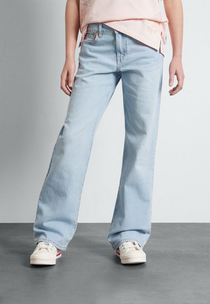 Světle modré široké džíny z denimu s vintage efektem praní a standardním designem s pěti kapsami, doplněné bílými teniskami.