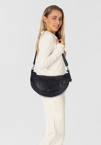Borsa a spalla in pelle nera con forma curva, tracolla regolabile e finitura testurizzata. Presenta un accento con il logo sulla parte anteriore.