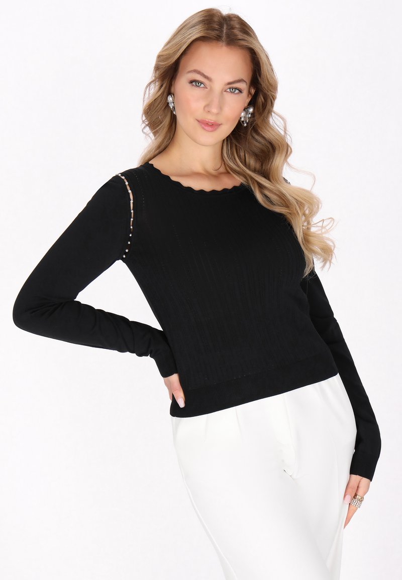 Pulover negru din tricot cu model canalat, cu decolteu în valuri și mâneci lungi, având aplicații pe o umăr. Asortat cu pantaloni albi.