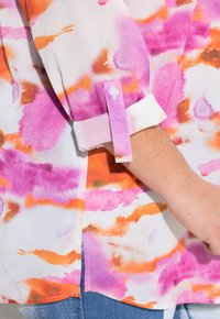 Blusa formal con un patrón de acuarela en tonos rosa, naranja y blanco. Presenta un puño con cierre de botón y una textura suave y lisa.