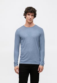 Sinised pikkade varrukatega särk pehmest kangast, millel on ümargune kaelus ja istuvad varrukad, kantud mustade pükstega. Minimalistlik disain.