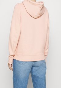 Różowa bluza z kapturem o miękkiej fakturze, z luźnym krojem, kapturem ze sznurkiem i ściągaczami na rękawach, zestawiona z jasno niebieskimi dżinsami.