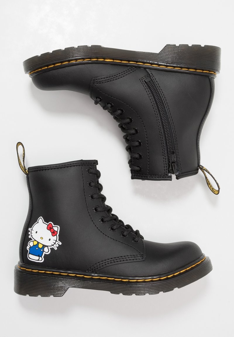 Černé kožené šněrovací boty s bočním zipem, žluté stehování na podrážkách a nášivka postavy Hello Kitty na vnější straně jedné boty.