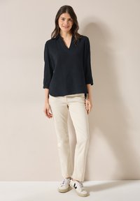 Top blu navy con texture, scollo a V e maniche a tre quarti, abbinato a pantaloni bianco sporco e sneakers bianche con accenti neri.