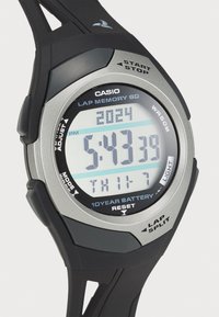 Montre numérique Casio avec un bracelet en résine noire et une lunette argentée. Dispose d'un affichage LCD clair affichant l'heure, la date et les fonctions. Résistante à l'eau.