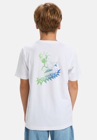 Bílý bavlněný tričko s grafickým potiskem na zadní straně, zobrazující stylizovanou postavu a text "Quiksilver" v zelených a modrých tónech.