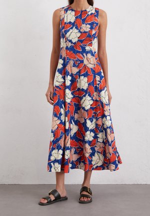 Bloemdeken met een blauwe basis en rode en roze bloemenpatronen, mouwloos ontwerp en een uitlopende zoom. Gecombineerd met zwarte sandalen.