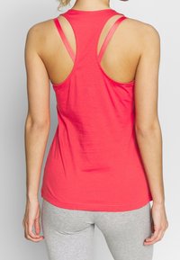 Top sin mangas de color rojo con corte racerback, hecho de una tela suave, que presenta tirantes estrechos y un ajuste holgado. La parte trasera es abierta con una textura suave.
