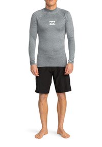 Camiseta de surf de manga larga en gris con un diseño ajustado y cuello redondo, combinada con pantalones cortos de baño negros. La camiseta cuenta con un pequeño logo.