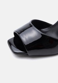 Μαύρο λουστρίνι mule με ανοιχτό δάχτυλο, φαρδιά λουρίδα και τετράγωνη μπροστινή όψη σε λευκό φόντο.